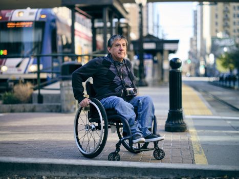 Man in a wheelchair waits at a tram stop