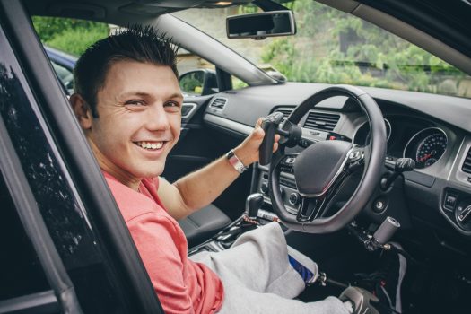 Quadriplegic man sitting in the seat of his customised control car. He is smiling for the camera.